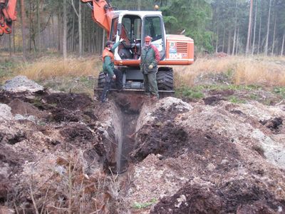 Mobilbagger hebt im Wald einen Graben aus