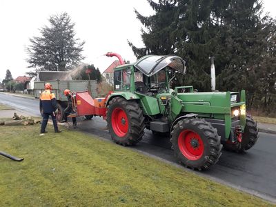 Fendt-Schlepper mit Häcksler, Mitarbeiter häckseln Astwerk am Straßenrand