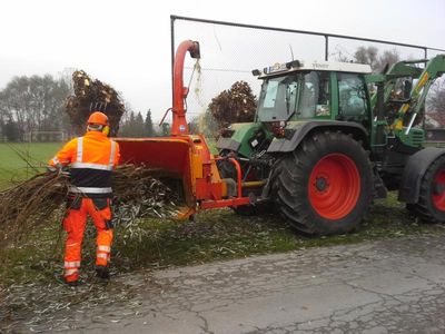 Mitarbeiter führt Astwerk in den Häcksler am Schlepper ein