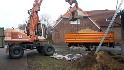 Mobilbagger setzt Betonringe für einen Regenwasser-Sickerschacht vor einem Wohnhaus