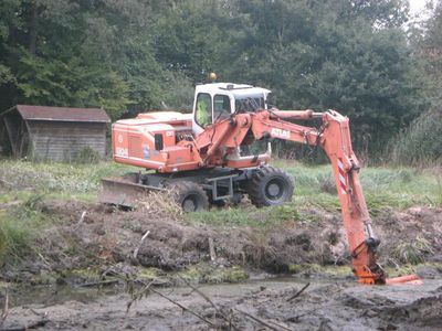 Mobilbagger hebt am Rand eines Teiches Schlamm aus