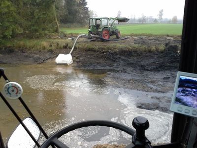 Blick aus der Baggerkabine auf den geräumten Teich, im Hintergrund ein Schlepper