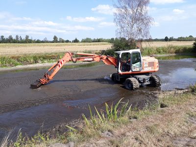 Mobilbagger steht im Teich und nimmt Schlamm auf